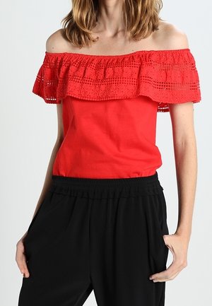 Czerwony top bez ramiączek z warstwowym koronkowym falbanem; gładka bawełniana tkanina; dopasowana góra; w komplecie z czarnymi spodniami na elastycznym pasie.
