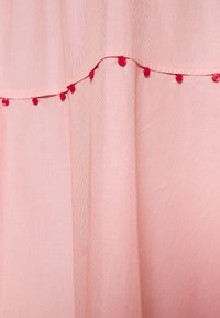 Tissu rose doux avec de délicats boutons rouges espacés régulièrement le long d'une couture horizontale, créant un détail décoratif subtil.