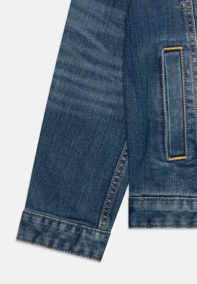 Giacca di denim in lavaggio blu scuro, caratterizzata da una tasca sul petto, dettagli in cucitura dorata e un texture leggermente sbiadita ai polsi e alle cuciture.