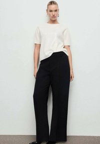 Top blanco de manga corta con un acabado texturizado, combinado con pantalones de tiro alto y pernera ancha negros, ambos con un diseño minimalista.