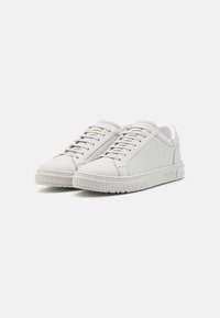 Zapatillas deportivas blancas de cuero con un acabado suave, puntera redondeada y suela de goma texturizada. Diseño minimalista con cordones planos y un acento de logo.