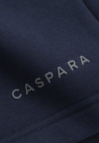 Mørkeblått stoff med en teksturert overflate som har ordet "CASPARA" i lys grått, plassert diagonalt over materialet.