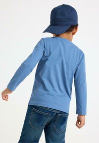 Lyseblå langærmet skjorte i bomuld, parret med mørkeblå denim jeans. Skjorten har et simpelt design og er lige skåret.