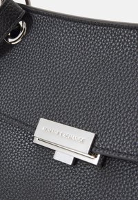 Czarna torebka skórzana o fakturze, z srebrnym zapięciem z wygrawerowanym napisem "Armani Exchange". Gładkie akcenty i uporządkowany kształt.