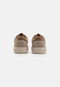 Hnědé tenisky s hladkou kůží a texturovaným svrškem, mají zaoblený tvar a béžovou gumovou podrážku. Minimalistický design bez viditelného loga.
