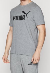Grå bomulds t-shirt med korte ærmer, der har et fremtrædende sort "PUMA" logo og et springende puma grafik henover brystet.
