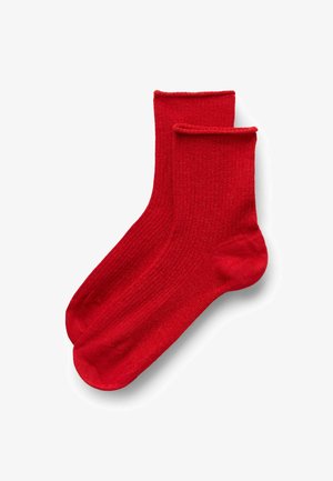 Un paio di calzini alla caviglia a righe di colore rosso brillante con polsini piegati su uno sfondo bianco.