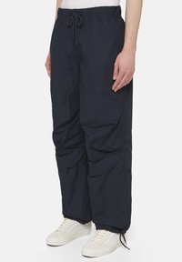Granatowe spodnie cargo z elastycznym pasem, sznurkiem, bocznymi kieszeniami i ściągaczami u dołu. Wykonane z lekkiego materiału, mają luźny krój.