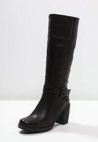 Botte noire montant jusqu'au genou en similicuir texturé, dotée d'un talon chunky et d'une boucle décorative autour de la cheville.