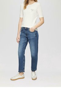 Camiseta blanca de manga corta con detalle de lazo, combinada con jeans de mezclilla azul. Corte clásico, diseño de pierna recta, zapatillas blancas con suelas beige.