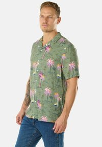 Camicia a maniche corte con colletto di colore verde oliva, decorata con vivaci motivi di palme in rosa, giallo e blu su un tessuto texture.