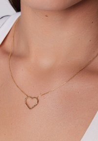 Naszyjnik z wisiorkiem w kształcie serca, pokryty złotem, o fakturowanym wykończeniu, zawieszony na delikatnym łańcuszku.