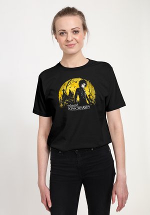 T-shirt en coton noir avec un graphisme jaune représentant un personnage entouré d'arbres, avec le texte "edward scissorhands" en blanc en dessous.