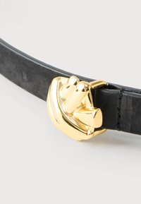 Cinturón de cuero negro con una hebilla dorada brillante que presenta un diseño audaz y abstracto sobre un fondo blanco.