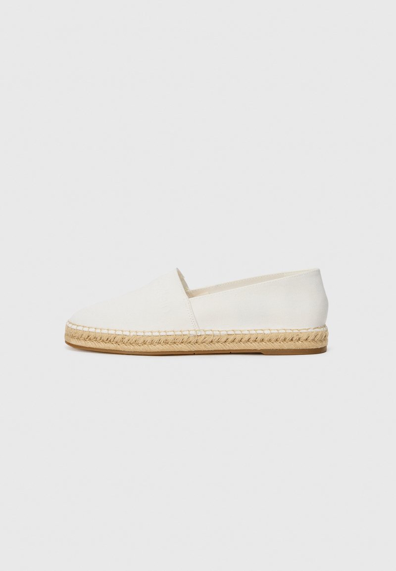 White canvas espadrille shoe with a woven jute sole and stitched detailing, featuring a slip-on design and minimalistic style.