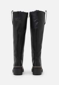 Bottes noires en cuir montantes avec une finition texturée, fermeture éclair et doublure en fourrure douce en haut. Comprend un talon large et robuste.