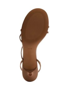 Brown flat sandal with a textured sole, featuring narrow straps. The design includes a round toe and a small circular opening at the front.
