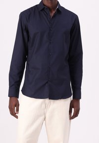 Navy blue long-sleeved button-up shirt with a collar, made from smooth fabric, featuring a straight hem and button closure down the front.