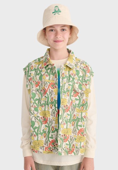 Młoda osoba nosząca kwiecistą kamizelkę na jasnej bluzce z długim rękawem oraz beżowy kapelusz typu bucket z zielonym napisem i grafiką „Pickles”.