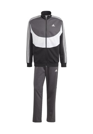 Tuta sportiva in nero e grigio con giacca con zip e pantaloni. Presenta strisce bianche sulle maniche e sui pantaloni, realizzata in materiale liscio e elasticizzato.