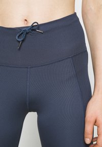 Námořnické modré žebrované legíny na cvičení s vysokým pasem, vybavené stahovací šňůrkou a plochými švy pro zvýšenou odolnost.