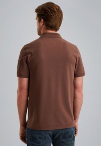 Hnedé polo tričko s krátkym rukávom, plochým golierom, detailom prešitého zadného panelu a bočnou vreckom na rukávu. Bavlnená látka.