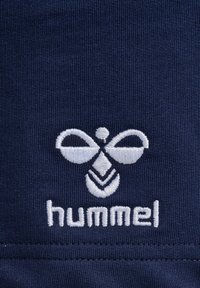 Navytyg har en vit broderad logotyp med en bi-liknande design ovanför texten "hummel", vilket framhäver textur och detaljer.