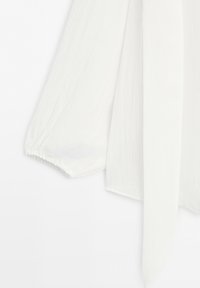 Witte blouse met lange mouwen van gestructureerde stof, met een losse mouw die eindigt in een elastische boord en een lange smalle strik die naar beneden hangt.