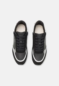 Paire de baskets BOSS noires et blanches avec design à lacets, en cuir suédé et cuir, vue de dessus sur un fond blanc.