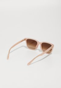 Óculos de sol rosa claro com armação quadrada, lentes de tom castanho e hastes texturizadas com um padrão subtil e detalhes em dourado.