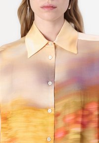 Silk blouse featuring a gradient of warm colors: yellow, orange, and subtle purple. Classic collar and white button details. Smooth texture.