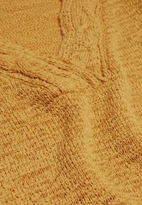 Gebreid dekbed in een levendige mosterdgele kleur, met een textuurpatroon en verhoogde kabeldetails. Zachte, warme en gezellige stofuitstraling.