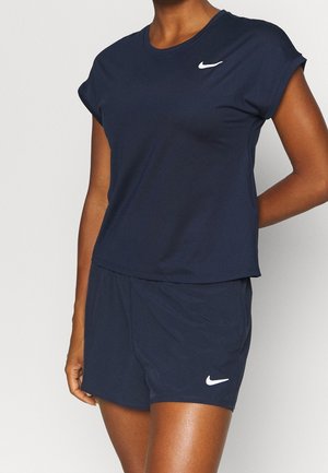 Osoba ubrana w granatową koszulkę Nike z krótkim rękawem i pasujące spodenki, oba z białym logo Nike Swoosh.