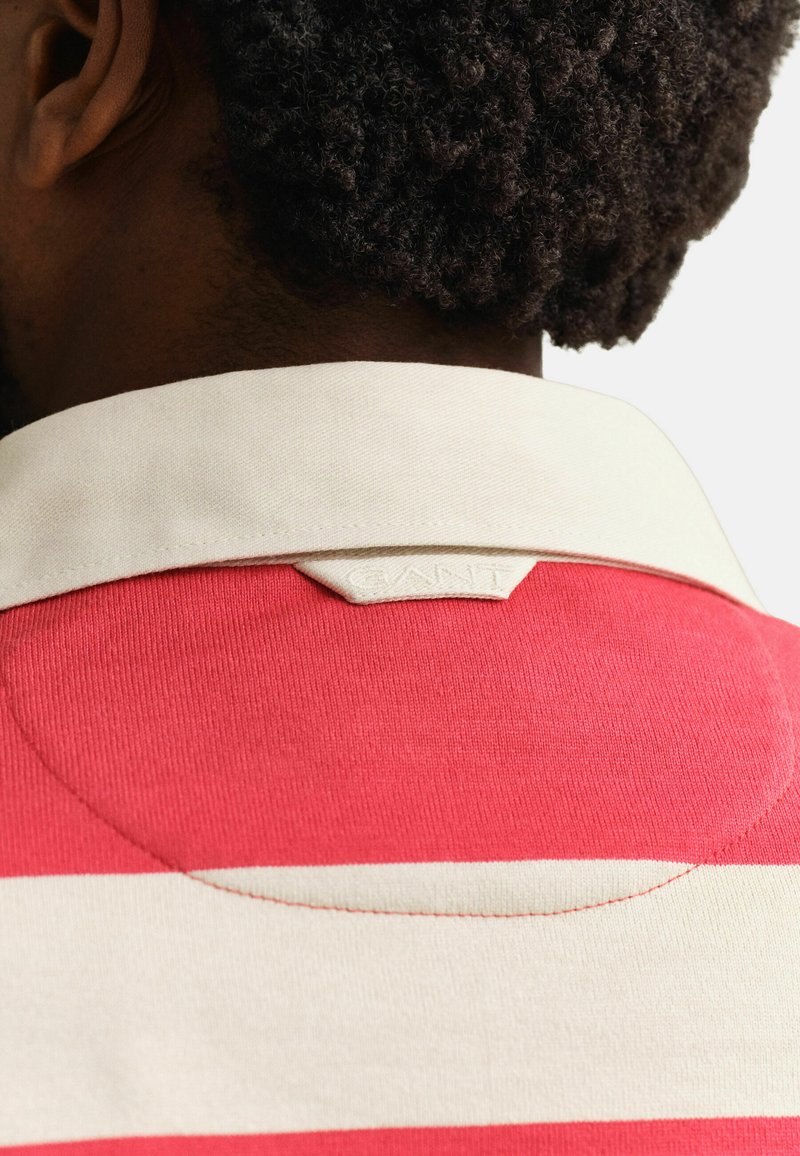 Nahaufnahme des Halses und der Schulter einer Person, die ein rot-weiß gestreiftes Hemd mit weißem Kragen und einem kleinen Stoffetikett auf der Rückseite trägt.