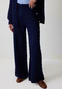 Marineblå kabelstrik brede benbukser med en ribbet talje og struktureret mønster. Sæt sammen med en lyseblå skjorte med knapper og brune loafers.