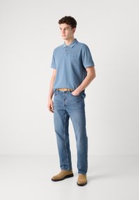 Cămașă polo albastru deschis cu un logo mic, asortată cu blugi din denim deschis și cizme scurte bej. Design simplu și croială lejeră.