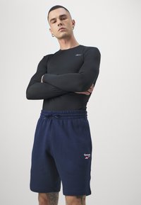 Fekete, hosszú ujjú sportpóló, amelyet sötétkék bolyhos rövidnadrággal párosítottak, rugalmas derékpánttal és egy kis Reebok logóval a szegélyén.