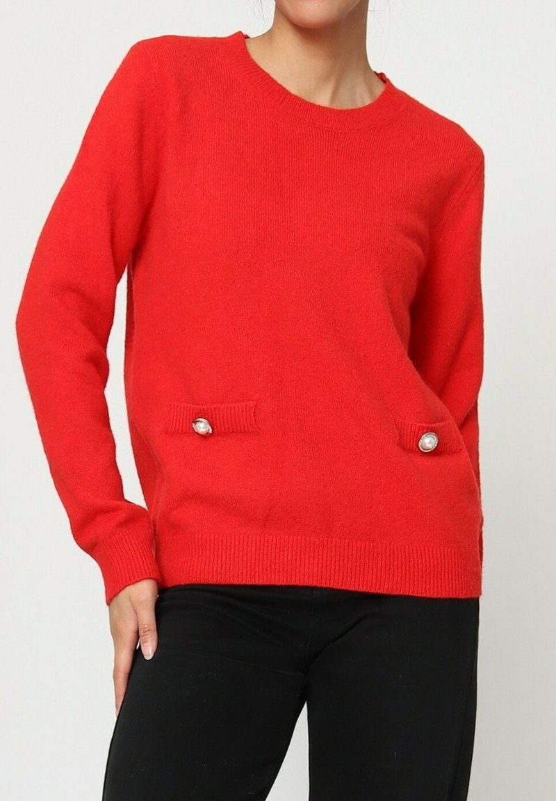 Pull en tricot rouge avec un col rond, comportant deux poches rehaussées de boutons décoratifs. Manches longues et coupe décontractée.