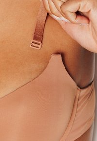 Reggiseno senza cuciture color carne con spallina regolabile in raso e chiusura a gancio. Tessuto morbido e liscio con finitura opaca. Etichetta della taglia visibile vicino al bordo.