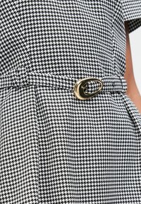 Μαύρο και λευκό φόρεμα καρό με ταιριαστό ζωνάκι που έχει οβάλ χρυσή αγκράφα στη μέση.