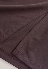 Primer plano de tela de color violeta oscuro con costuras visibles y bordes doblados que se superponen.