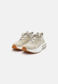 Beige athletic shoes with a breathable mesh upper, textured detailing, and a rubber sole. Features lace-up closure and a pull tab.