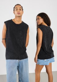 Črne brezrokavnike iz bombaža z zbledelim vzorcem, okroglim izrezom in sproščenim krojem. Ujemajo se z svetlo modrimi jeans kratkimi hlačami.