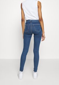 Höga, blå denimjeans med en figurnära silhuett, utrustade med två bakfickor och en slät textur. Bärs med vita sneakers.