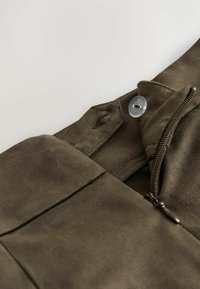 Hnědá umělá semišová látka se zipovým zapínáním, detaily s knoflíkem a hladkým povrchem. Obsahuje elegantní, upravenou siluetu.