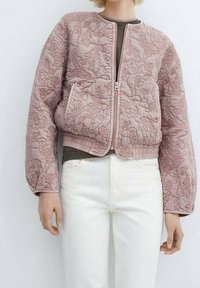 Giacca bomber rosa trapuntata con ricami floreali, zip frontale, due tasche laterali e polsini a coste, abbinata a pantaloni chiari.