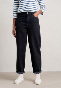 Jeans de tiro alto azul oscuro con un corte relajado, con los puños enrollados, combinados con zapatillas blancas. Camisa de manga larga a rayas llevada por encima.