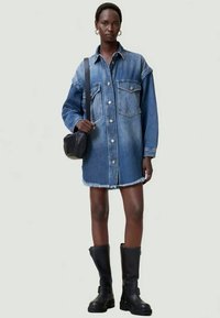 Denim srajčna obleka v svetlo modri barvi z dolgimi rokavi, gumbom spredaj, dvema žepoma na prsih in strganim robom. V kombinaciji z črnimi gležnjarji in torbico čez ramo.