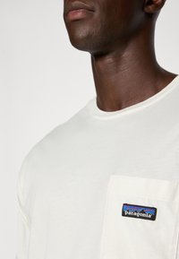 White, short-sleeve t-shirt made of cotton. Features a left chest pocket with a multi-colored Patagonia logo patch. Smooth texture.