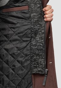 Smeđa vanjska površina s sivim, teksturiranim unutrašnjim dijelom i crnom, kviltanom podlogom. Ima zatvarač i tkaninski džep.